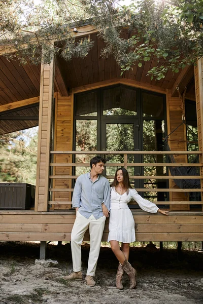 Модна романтична пара в повсякденному одязі, що стоїть під деревами біля будинку відпочинку на відкритому повітрі — стокове фото