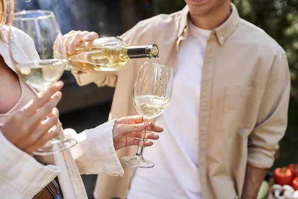 Cropped view of man pouring wine in glasses near blurred girlfriend during picnic outdoors — Stock Photo