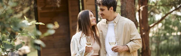 Cheerful love couple with glasses of wine spending time during picnic near vacation house, banner — Stock Photo