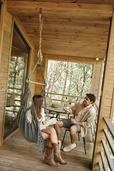 Позитивная романтическая пара с вином и едой разговаривает и проводит время на террасе летнего дома — стоковое фото
