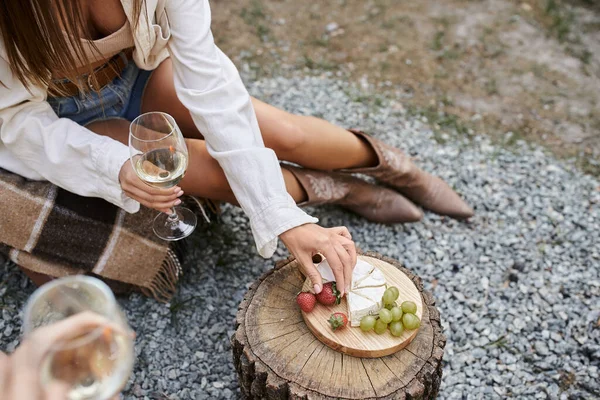High angle view of young woman holding wine and taking fruits near cheese and boyfriend outdoors — Stock Photo