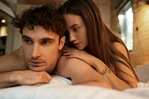 Jeune femme tatouée et sexy touchant torse nu petit ami sur le lit dans la maison de vacances floue — Photo de stock