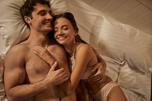 Vista dall'alto di coppia sorridente e sexy con gli occhi chiusi sdraiati sul letto in casa di vacanza in serata — Foto stock