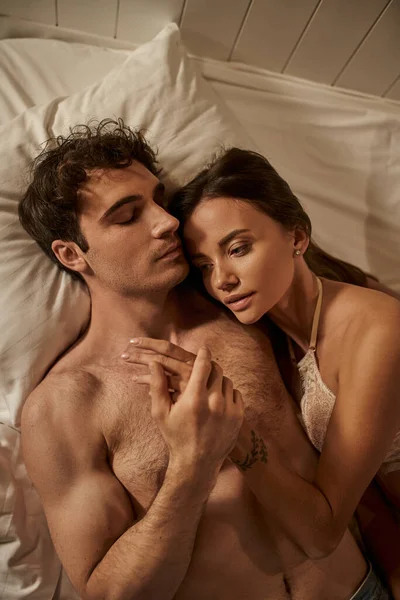 Vue du dessus de la femme sexy en lingerie toucher la main du copain torse nu sur le lit dans la maison de vacances — Photo de stock
