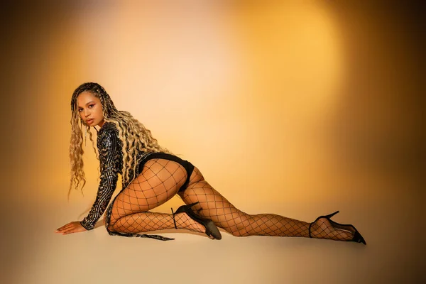 Seductive african american woman crawling on yellow background, sexy fishnet tights, high heels — Stock Photo
