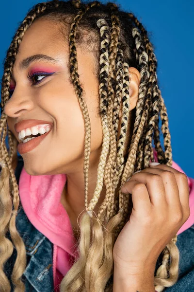 Vicino, donna afro-americana positiva sorridente e distogliendo lo sguardo su sfondo blu, trucco audace — Foto stock