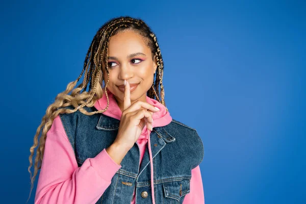 Sorrindo mulher americana africana com dreadlocks mostrando sinal de silêncio, fundo azul, dedo perto de lábios — Fotografia de Stock