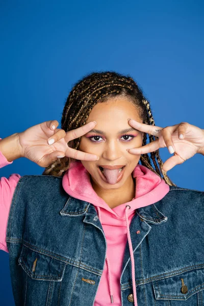 Африканская американка с дредами показывает V знак с руками и торчащий язык на синий — стоковое фото