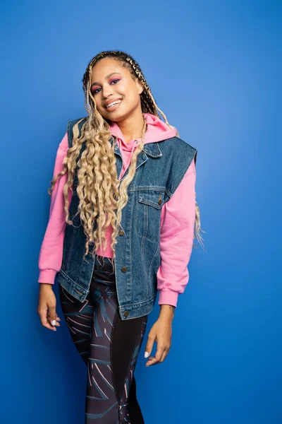 Pretty woman with dreadlocks standing in leggings and pink hoodie on blue background, diversity — Stock Photo