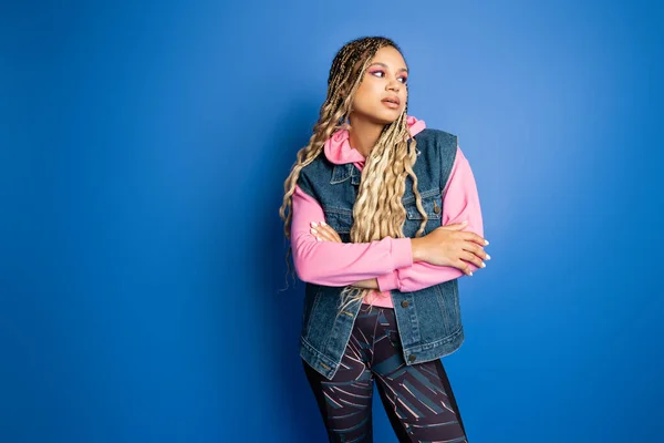 Confident african american woman with dreadlocks posing and looking away on blue background — Stock Photo