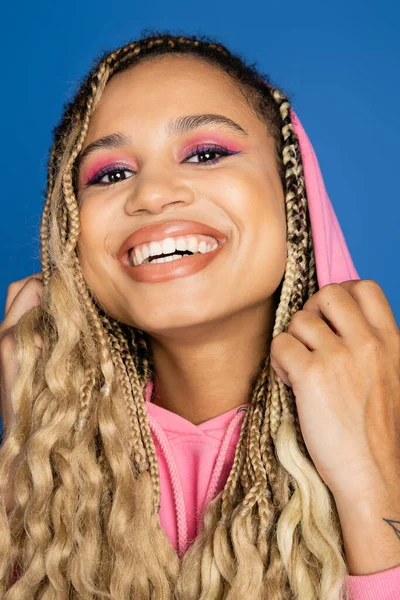 Portrait de femme noire joyeuse avec capuche sur la tête regardant la caméra et souriant sur fond bleu — Photo de stock