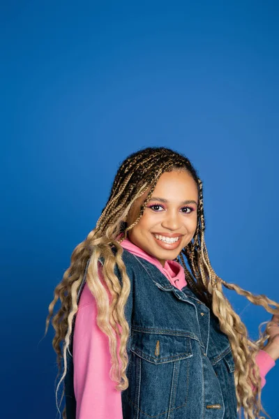 Portrait, happy dark skinned woman standing on blue background, denim vest and pink hoodie, smile — Stock Photo