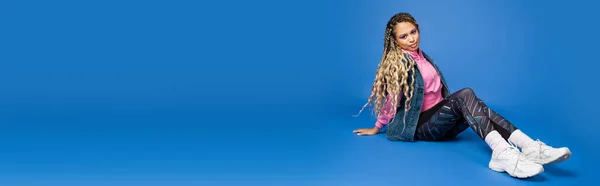 Comprimento total de cabelos longos mulher americana africana em roupas esportivas sentado em azul, banner — Fotografia de Stock