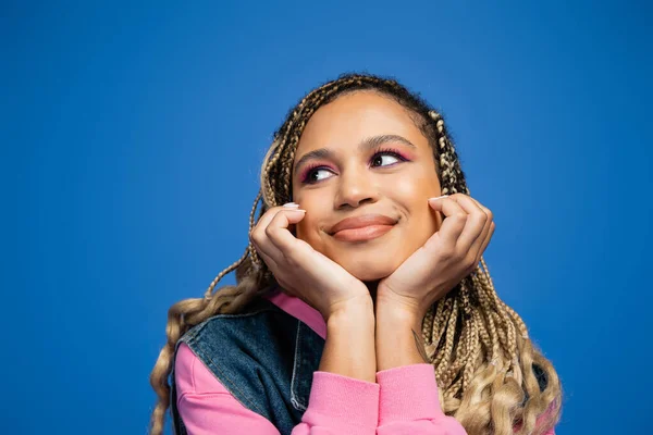Porträt einer glücklichen und verträumten afrikanisch-amerikanischen Frau mit kühnem Make-up auf blauem Hintergrund — Stockfoto