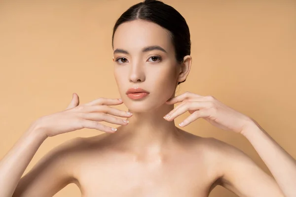 Jeune femme asiatique avec maquillage naturel touchant le visage et regardant la caméra isolée sur beige — Photo de stock