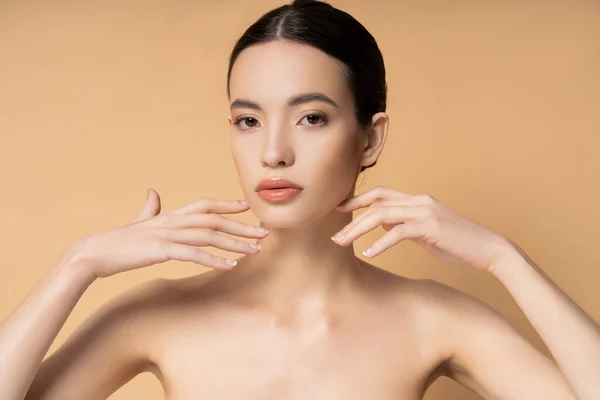 Young asian woman with natural makeup touching face and looking at camera isolated on beige — Stock Photo