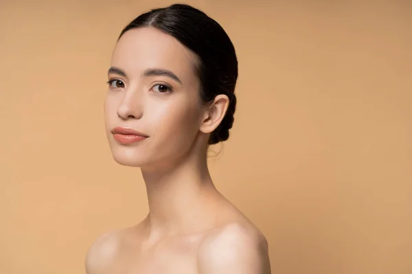 Young asian woman with naked shoulders and natural makeup looking at camera isolated on beige — Stock Photo