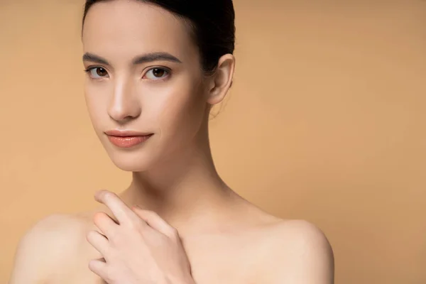 Portrait of young asian brunette woman with naked shoulders and natural makeup isolated on beige — Stock Photo