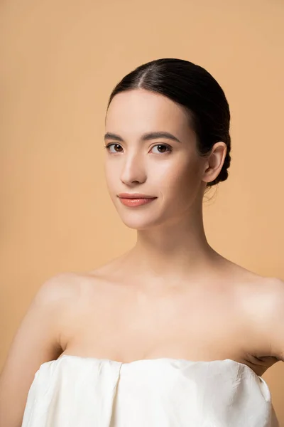 Young brunette asian woman in top with naked shoulders looking at camera isolated on beige — Stock Photo