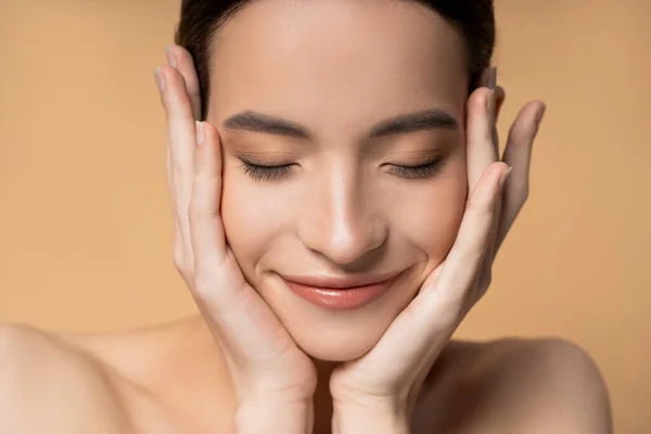 Close up view of asian woman with closed eyes and naked shoulders touching face isolated on beige — Stock Photo