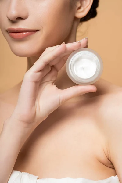 Cropped view of young woman in top holding cosmetic cream and standing isolated on beige — Stock Photo