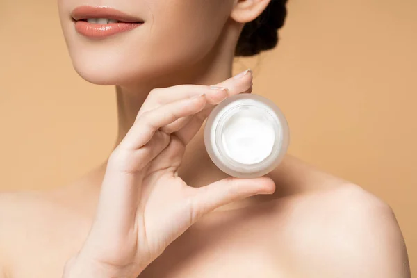 Cropped view of smiling young woman with naked shoulders holding cosmetic cream isolated on beige — Stock Photo