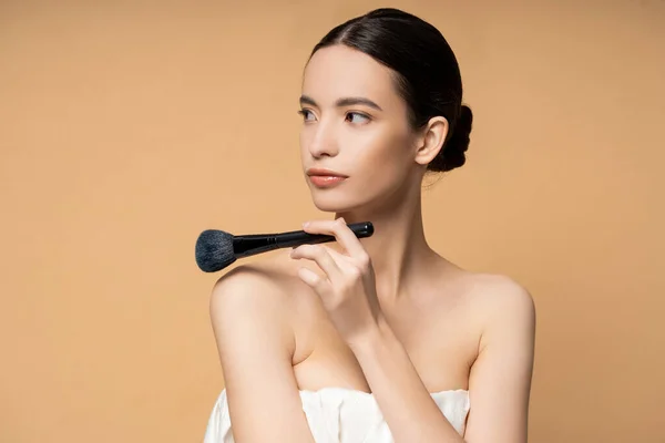 Young asian woman in top holding blush brush near naked shoulders isolated on beige — Stock Photo