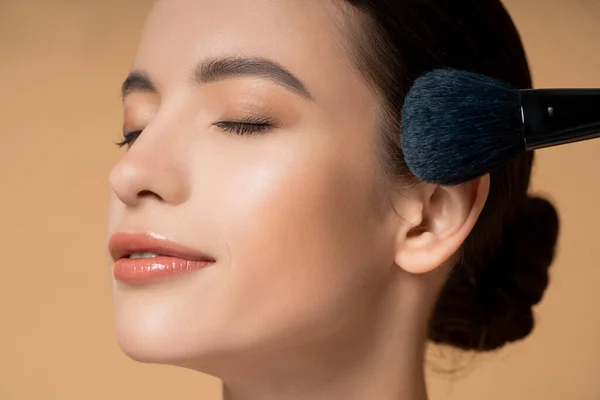 Maquillaje cepillo cerca de joven morena mujer asiática con rostro natural aislado en beige - foto de stock