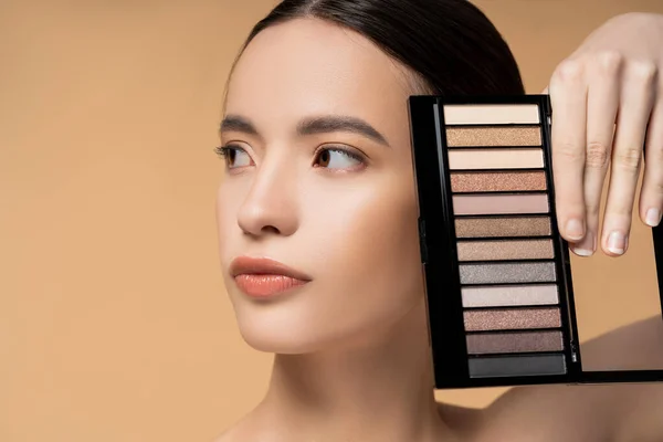 Porträt einer jungen asiatischen Frau mit natürlichem Make-up mit Lidschatten-Palette isoliert auf beige — Stockfoto