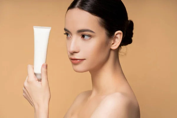 Jeune modèle asiatique avec des épaules nues tenant lotion cosmétique tout en posant isolé sur beige — Photo de stock