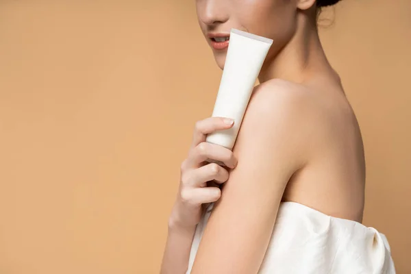 Cropped view of young smiling woman in top holding cosmetic lotion in tube isolated on beige — Stock Photo