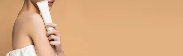 Vue recadrée d'une femme souriante avec épaule nue tenant un baume cosmétique isolé sur beige, bannière — Photo de stock