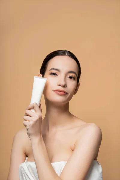 Portrait de jeune modèle asiatique en haut tenant le baume cosmétique et regardant la caméra isolée sur beige — Photo de stock