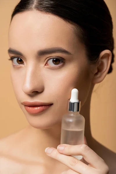 Close up vista de jovem mulher asiática com pele perfeita segurando soro cosmético isolado no bege — Fotografia de Stock