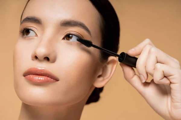 Junges asiatisches Model mit natürlichem Make-up und perfekter Haut mit Mascara-Applikator auf Beige isoliert — Stockfoto