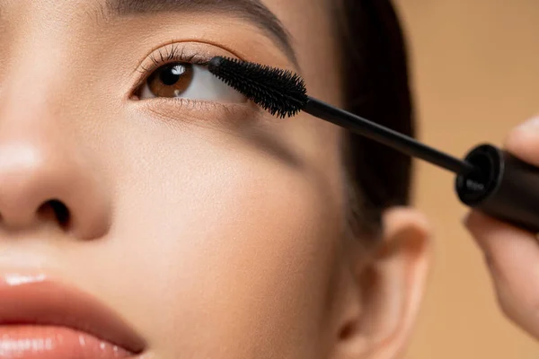 Close up view of young asian woman with natural makeup applying mascara on lushes isolated on beige — Stock Photo