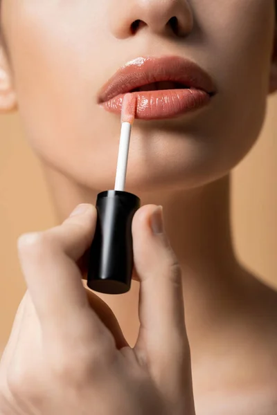 Ausgeschnittene Ansicht einer jungen Frau, die Lipgloss aufträgt, während sie sich isoliert auf Beige schminkt — Stockfoto