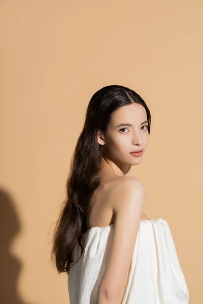Jolie jeune modèle asiatique aux cheveux longs en haut regardant la caméra sur fond beige avec ombre — Photo de stock