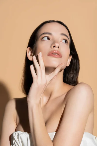 Jolie jeune femme asiatique au visage naturel touchant menton sur fond beige avec ombre — Photo de stock