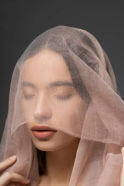 Porträt einer jungen und schönen asiatischen Frau mit beigem Tuch auf dem Kopf, die isoliert auf grau steht — Stockfoto