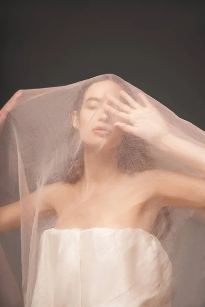 Young asian woman in top with naked shoulders posing under beige cloth isolated on grey — Stock Photo
