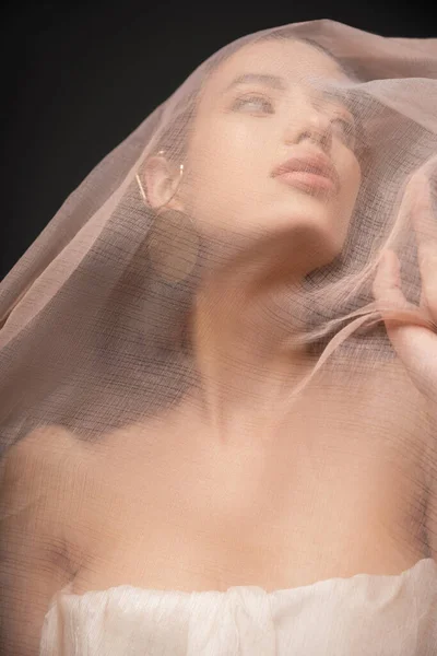 Baixo ângulo vista de jovem modelo asiático com ombros nus olhando para longe sob pano isolado em preto — Fotografia de Stock