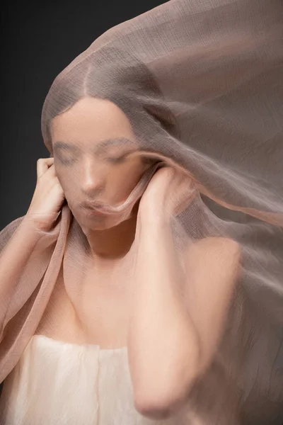 Ritratto di giovane modella asiatica con gli occhi chiusi che tiene il tessuto beige e sta isolata sul nero — Foto stock