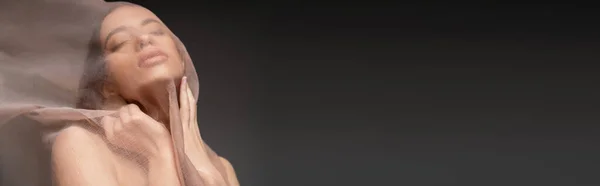 Modello asiatico con gli occhi chiusi posa sotto panno beige mentre in piedi isolato su nero, striscione — Foto stock