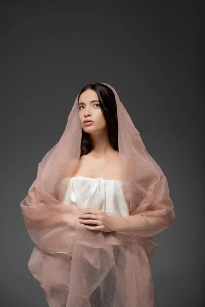 Giovane bruna modello asiatico in alto in posa in tessuto beige mentre posa isolata sul grigio — Foto stock