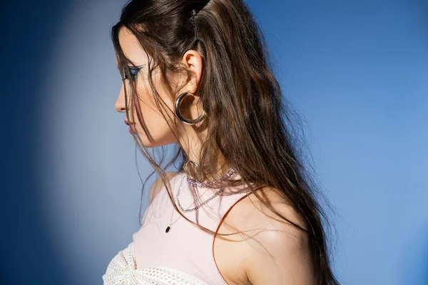 Vista lateral de joven modelo asiático con peinado y maquillaje atrevido posando sobre fondo azul - foto de stock