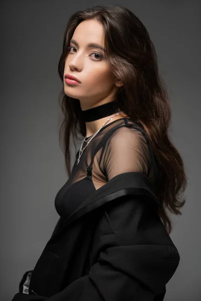Porträt einer asiatischen Frau in stylischem Netztop und schwarzer Jacke, die isoliert auf grau in die Kamera blickt — Stockfoto
