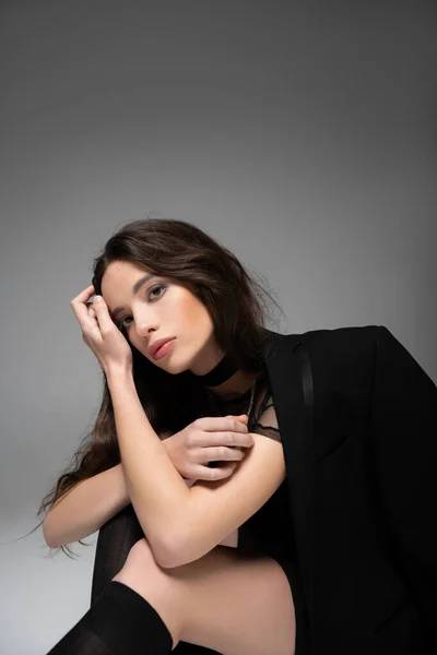 Модная молодая азиатская модель в сетчатом топе и черной куртке, смотрящая на камеру, изолированную на сером — стоковое фото