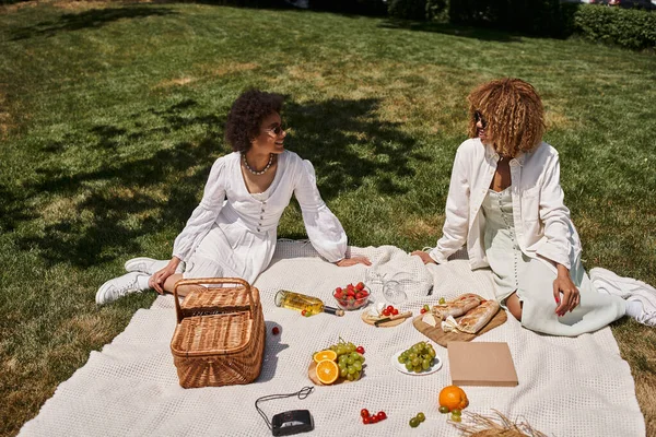 Fidanzate afro-americane positive vicino alla frutta, verdure sulla coperta, picnic estivo — Foto stock