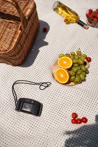 Summer picnic concept, food, bottle, wine, wicker basket, oranges, grapes, vintage camera, top view — Stock Photo